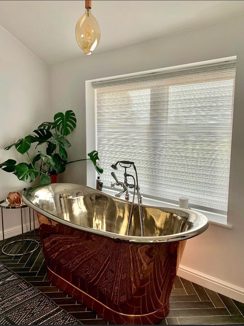 Roller blind next to brass bath tub